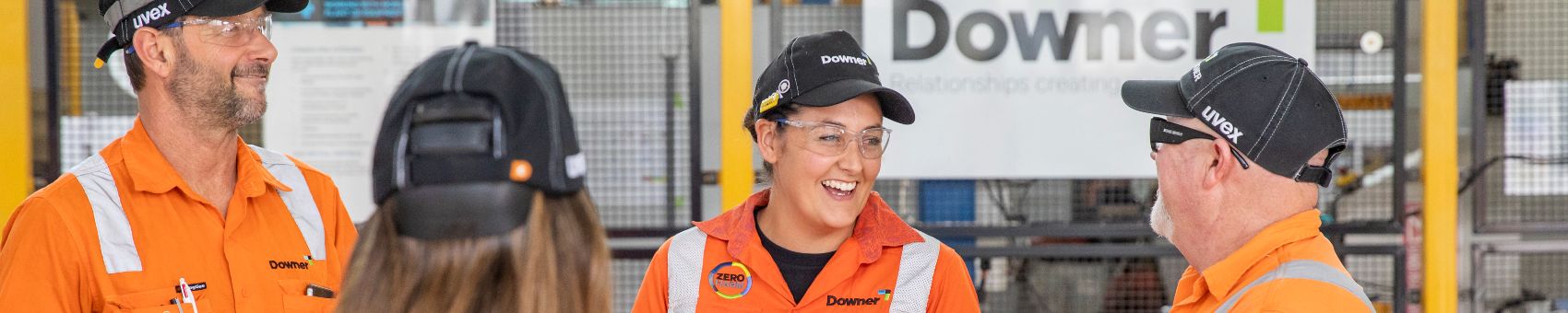 Four Downer employees in high vis stand together. They are laughing.